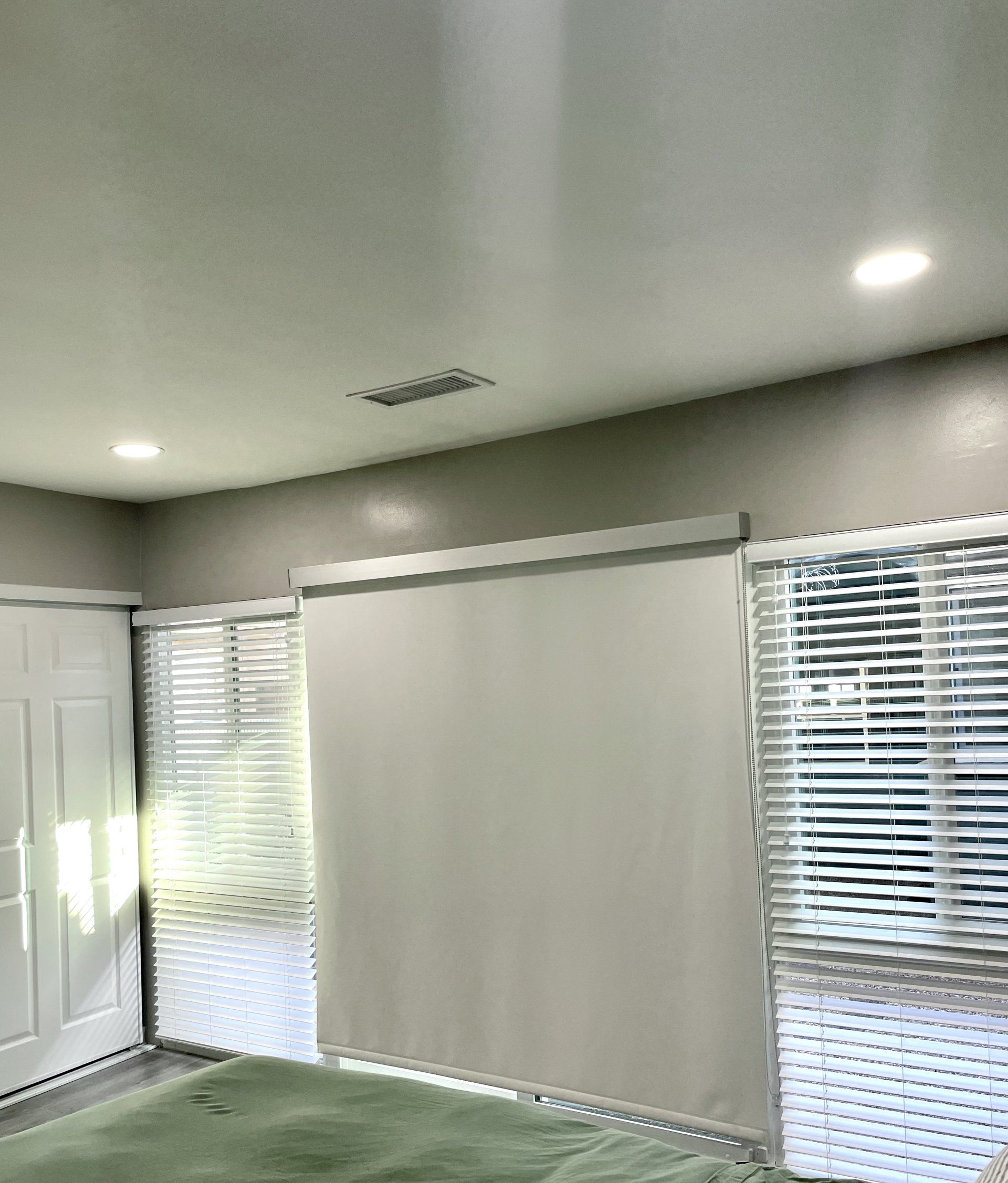 A bedroom with blinds on the windows and a green rug.