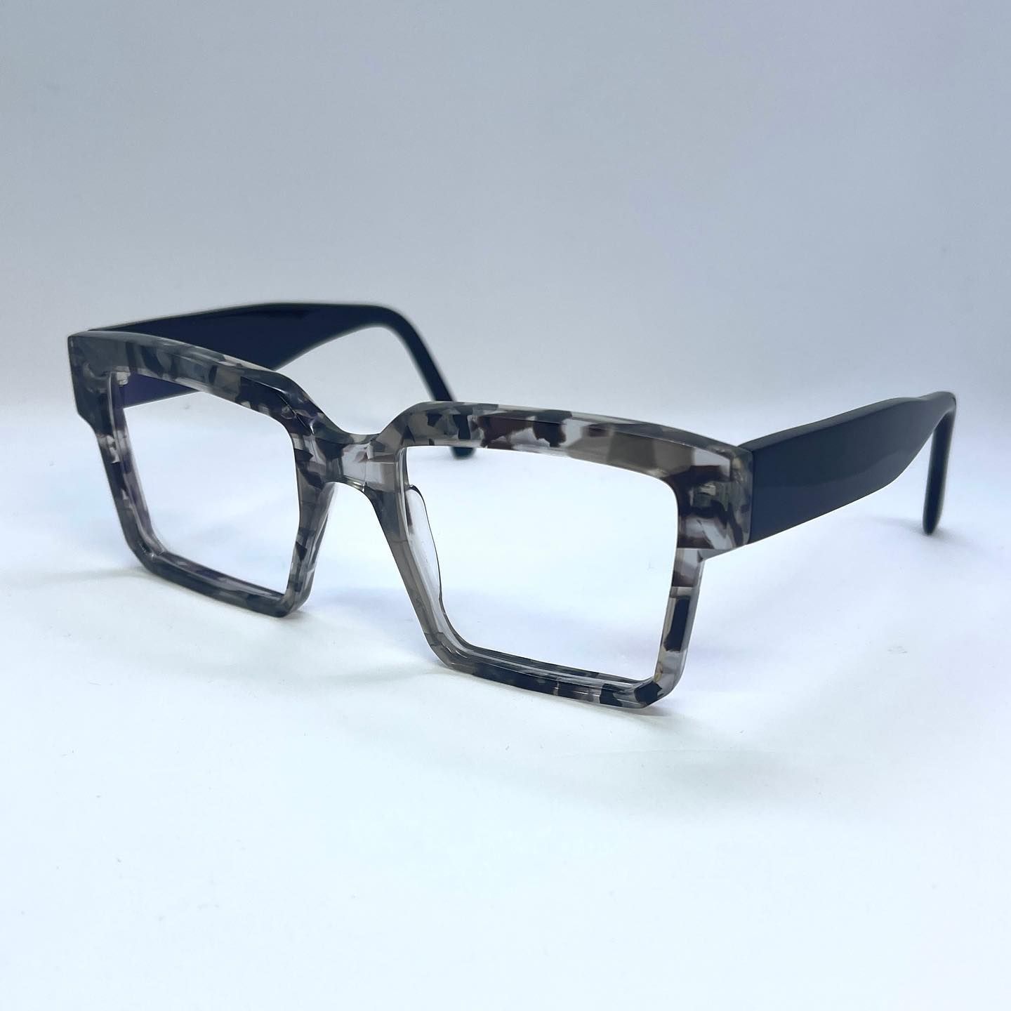 A pair of chunky acetate glasses are sitting on a white surface.