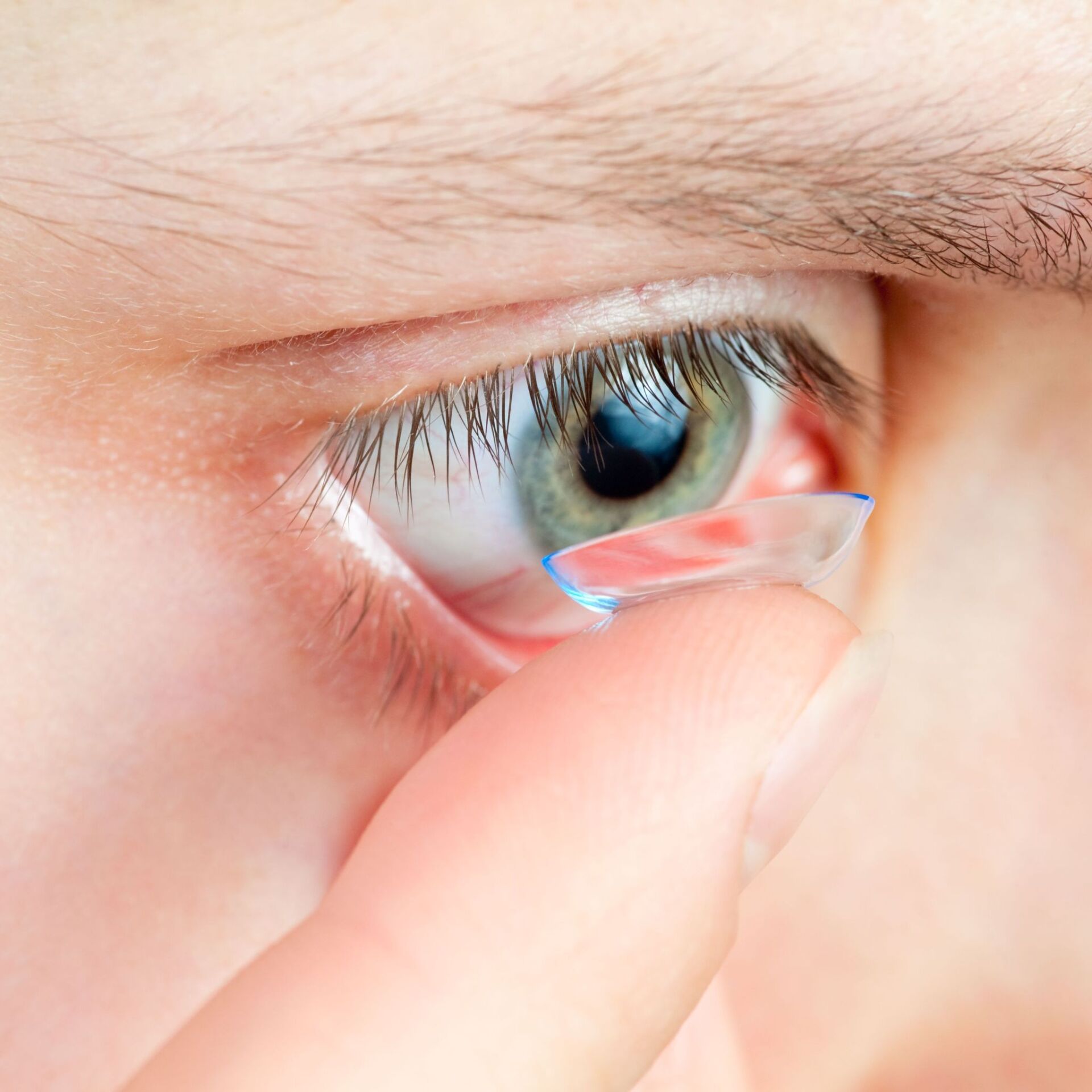 Close up of a person inserting a contact lens into right eye