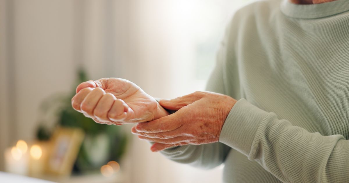 A person in a light green sweater holds their wrist with their other hand, suggesting pain or discomfort.