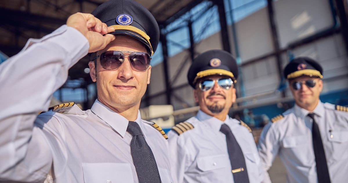 Three pilots are standing next to each other wearing aviator sunglasses and hats.