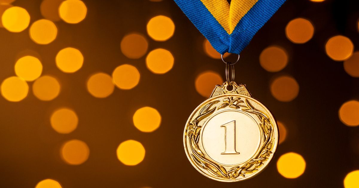 A gold medal with the number 1 on it is hanging from a blue and yellow ribbon.