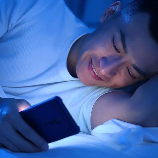 A man is lying in bed looking at his cell phone.