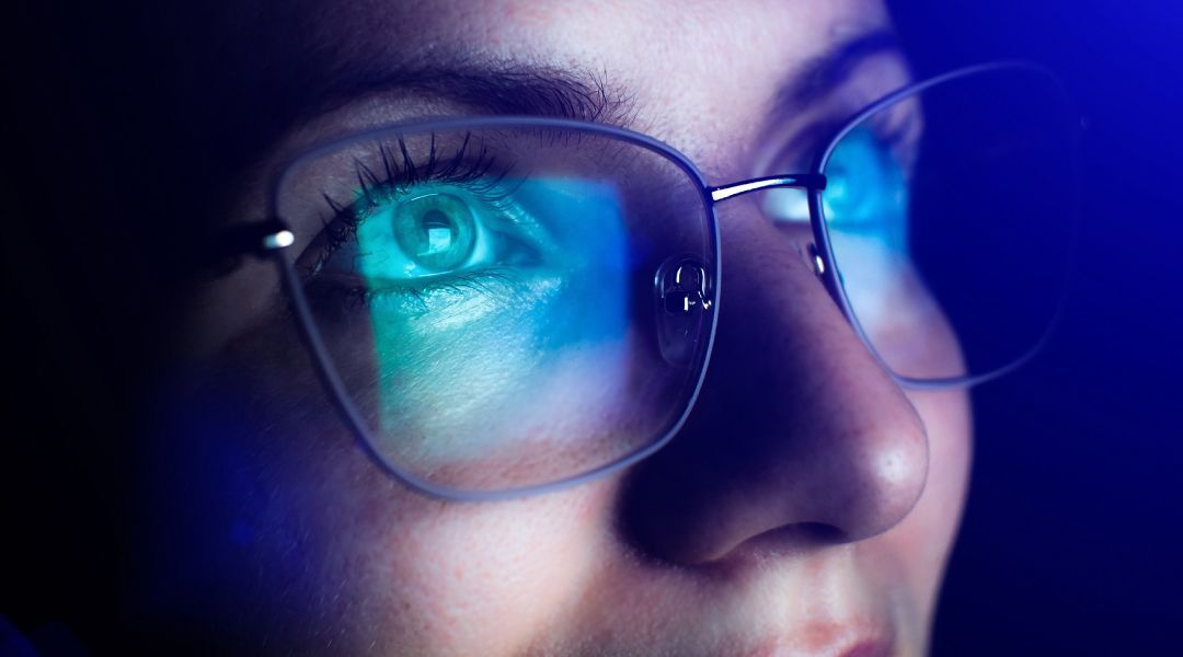 Close up of a person wearing glasses with a blue tint reflecting on them.