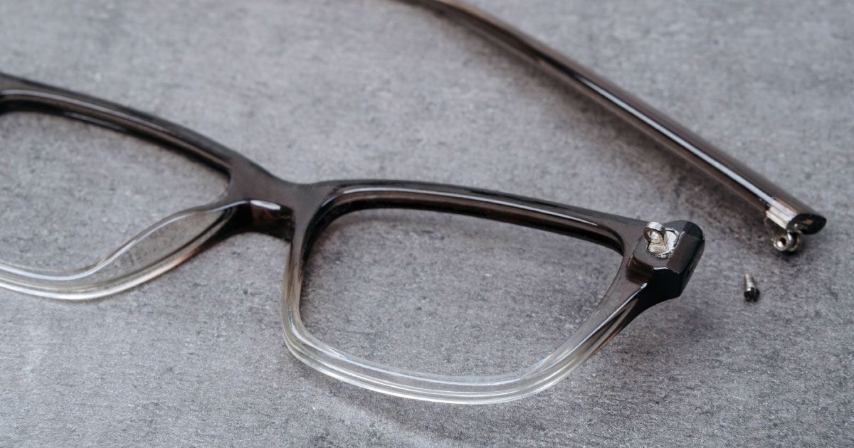 A pair of glasses with a broken frame is laying on a table.