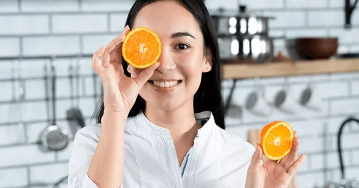 A woman is holding a slice of orange in front of her eyes.