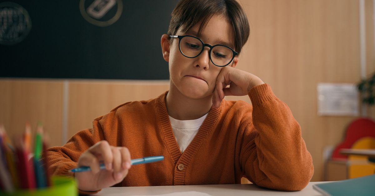 A young boy is sitting at a desk studying in a classroom holding a pen.