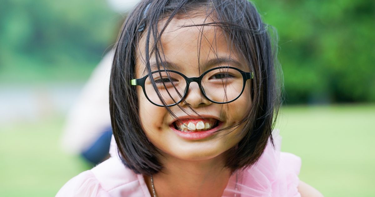 A little girl wearing glasses smiling for the camera.