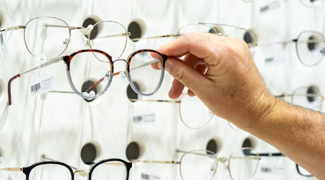 Close up of a hand selecting glasses off a wall of frames