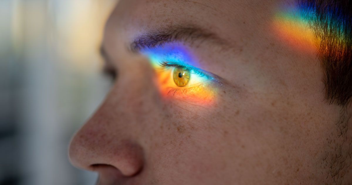 A close up of a man 's eye with a rainbow reflected in it.