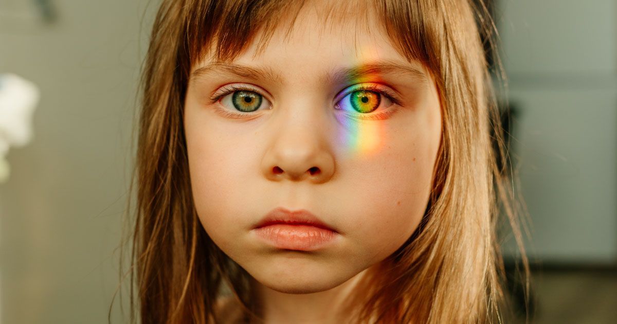 A little girl with a rainbow reflected in her  left eye.