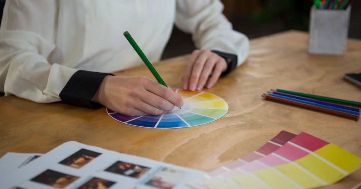 A woman sitting at a table drawing a color wheel with a pencil.