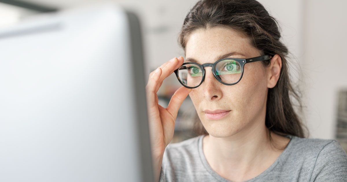 A woman wearing glasses is looking at a computer screen.