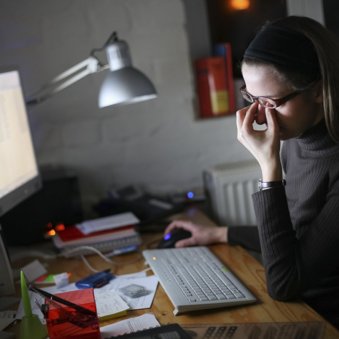 Woman rubbing her eyes as she sits at a desk with a computer
