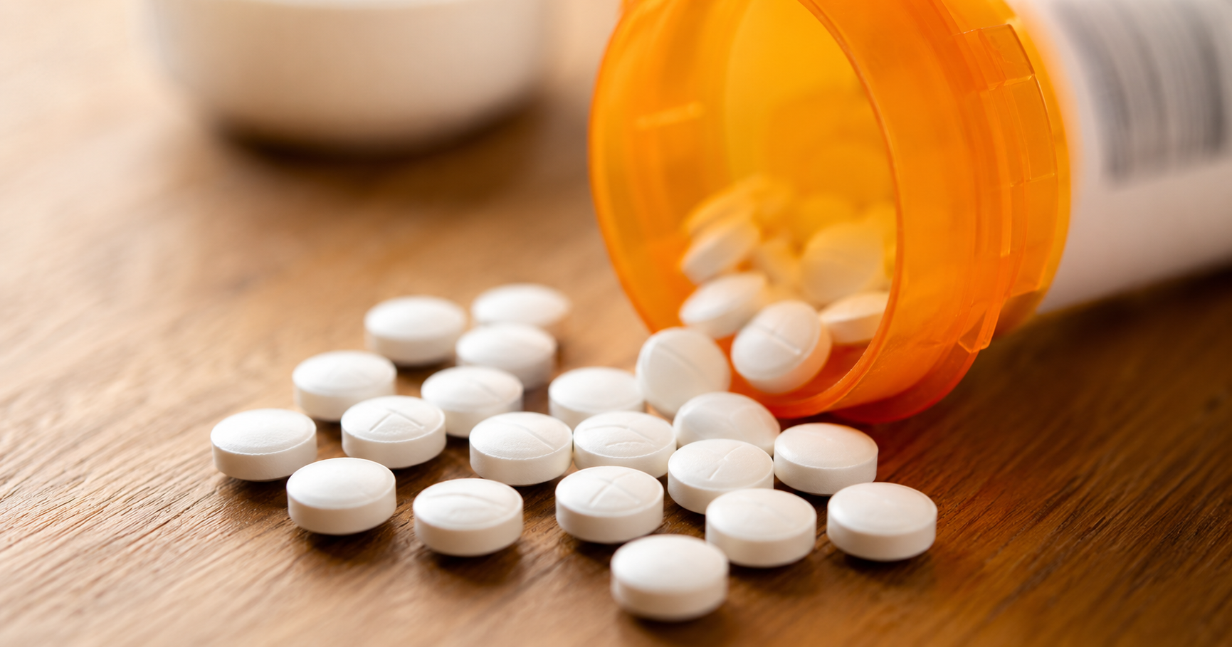 Spilled white tablets from an orange prescription bottle on a wooden surface