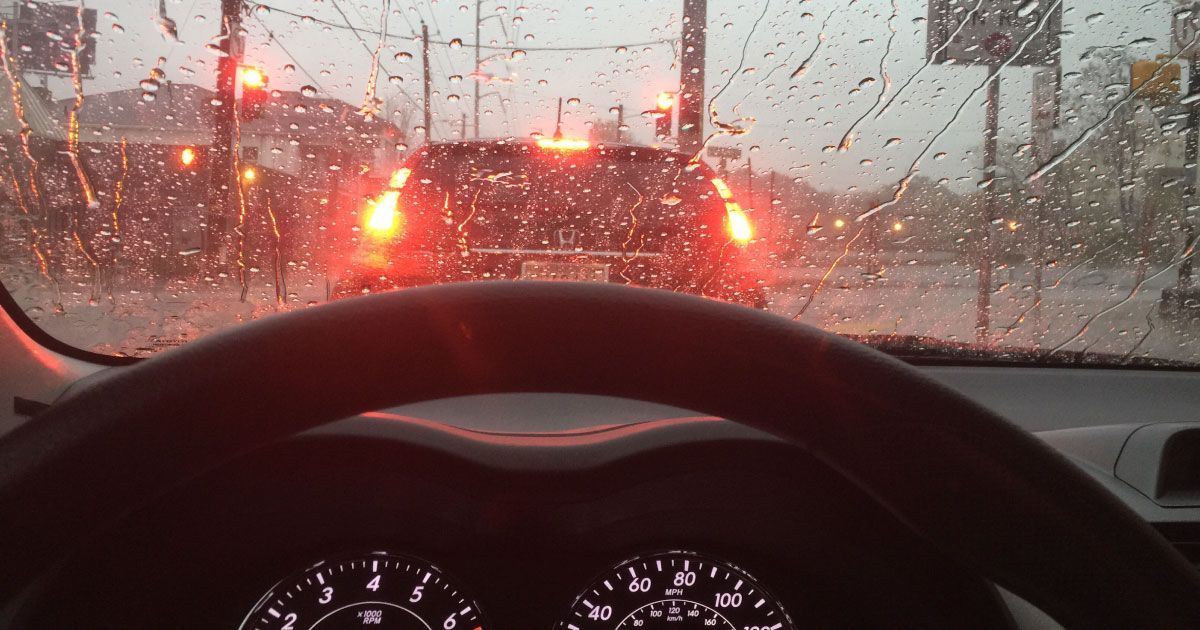 A car is driving down a wet street in the rain.