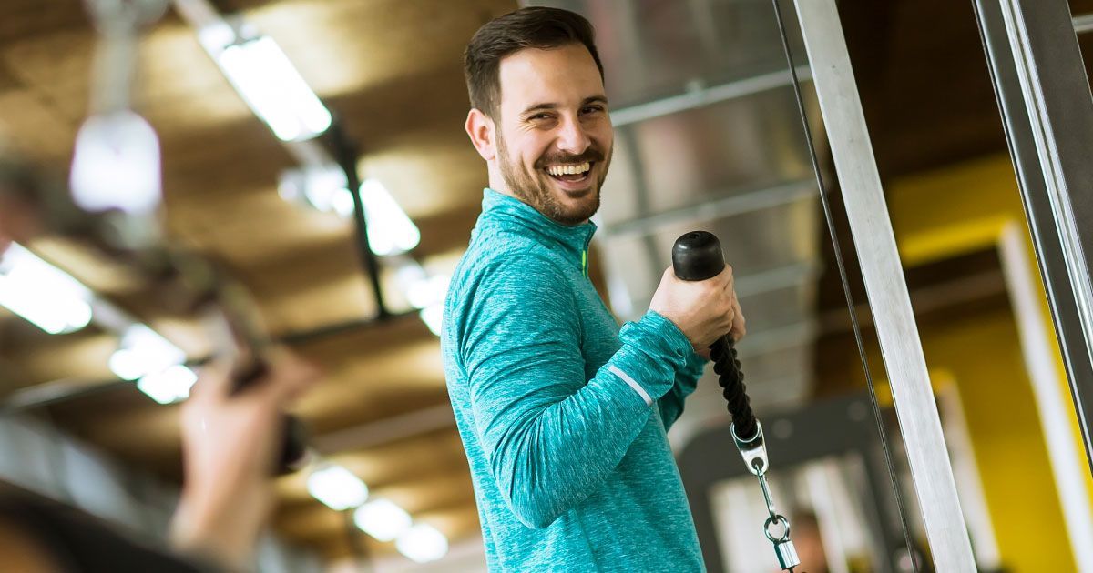 A man is smiling while using a weight machine in a gym.