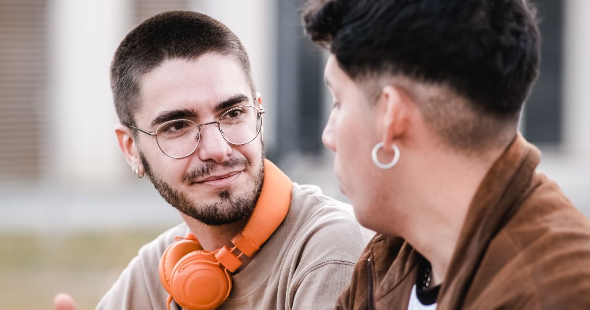 A man wearing headphones is talking to another man.