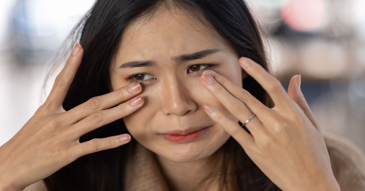 A woman is rubbing her eyes with her hands while crying.