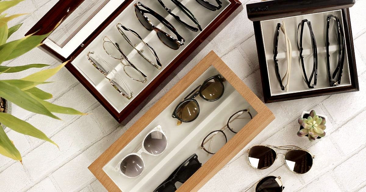 Three covered eyewear storage cases filled with glasses and sunglasses are sitting on a table.