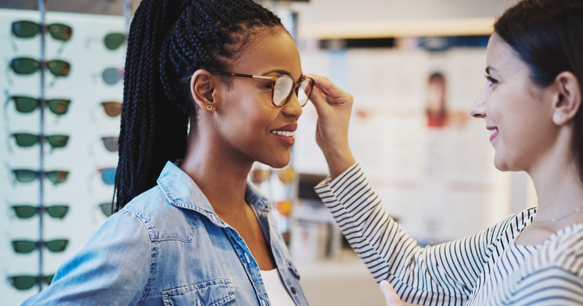 An optician is adjusting a patient's glasses on her head.