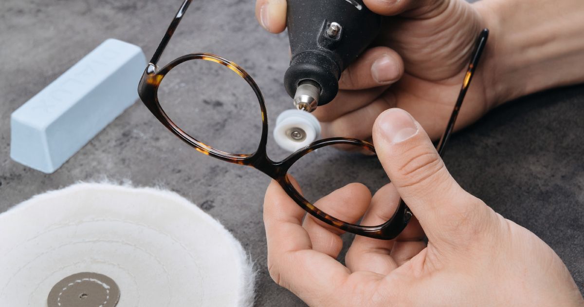 A person is polishing a pair of vintage tortoise shell glasses with a machine.