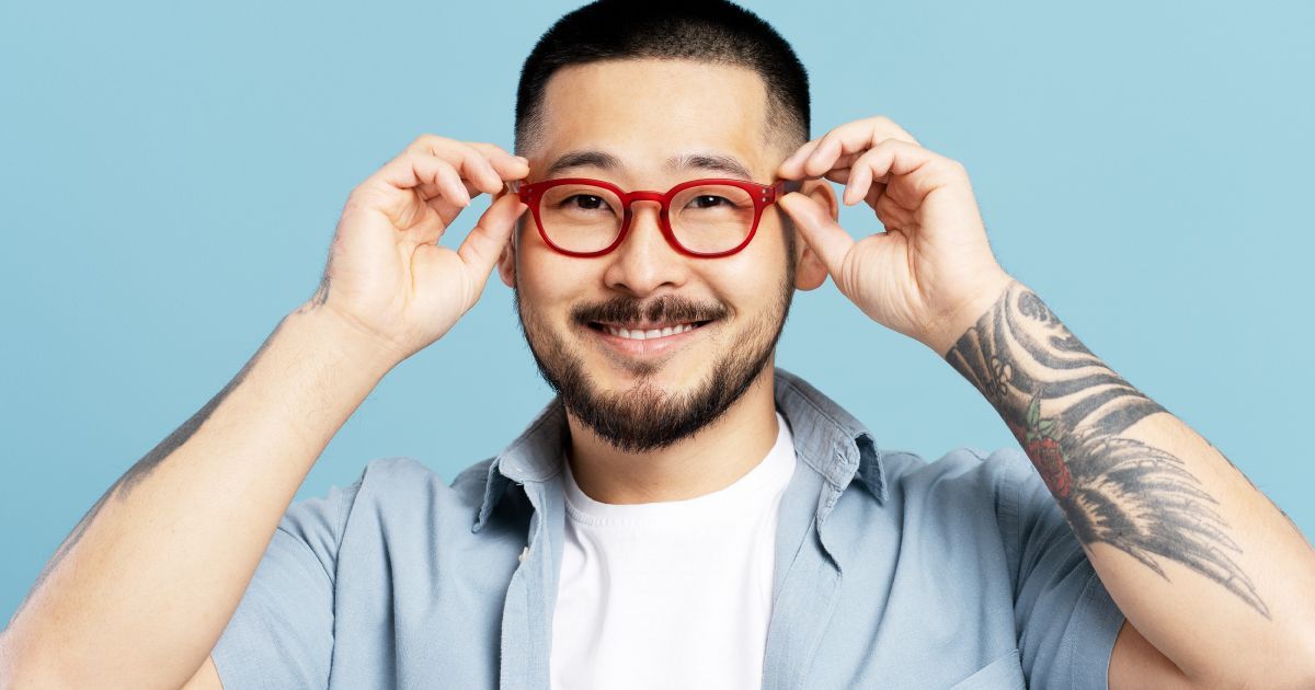 A man with a tattoo on his arm is placing a pair of red glasses on his head.