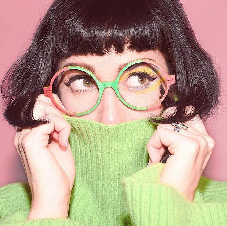Woman in a turtleneck wearing  a green and pink pair of glasses