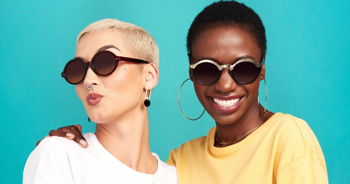 Two women in sunglasses and fashionable accessories, smiling and posing together.