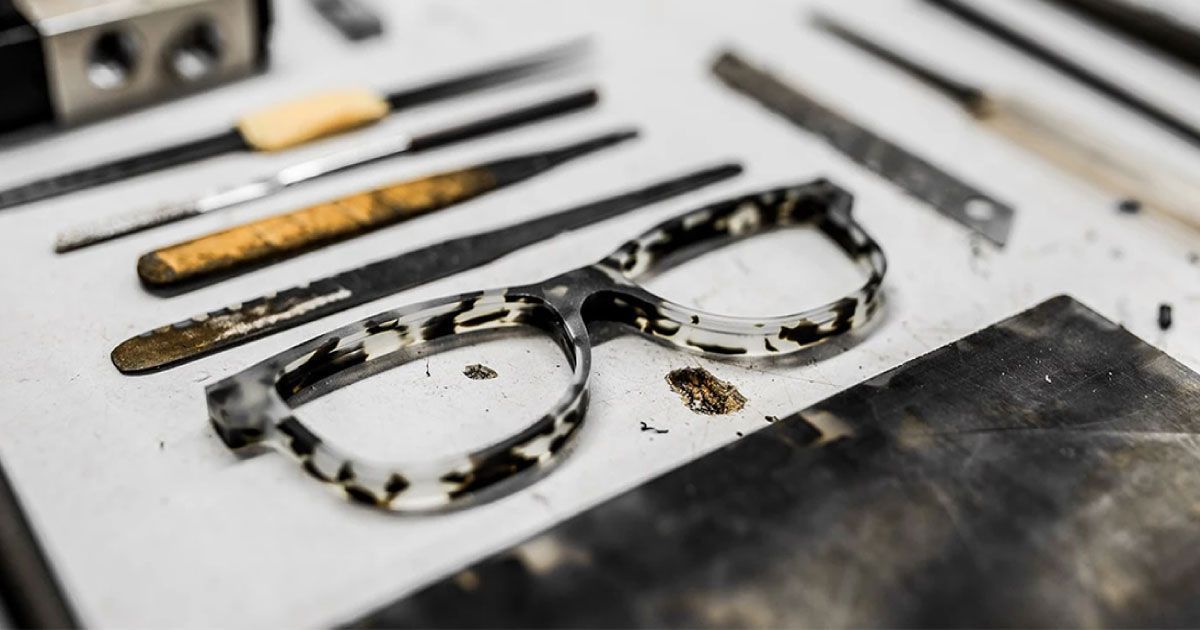 A pair of glasses being constructed is sitting on a table next to tools.