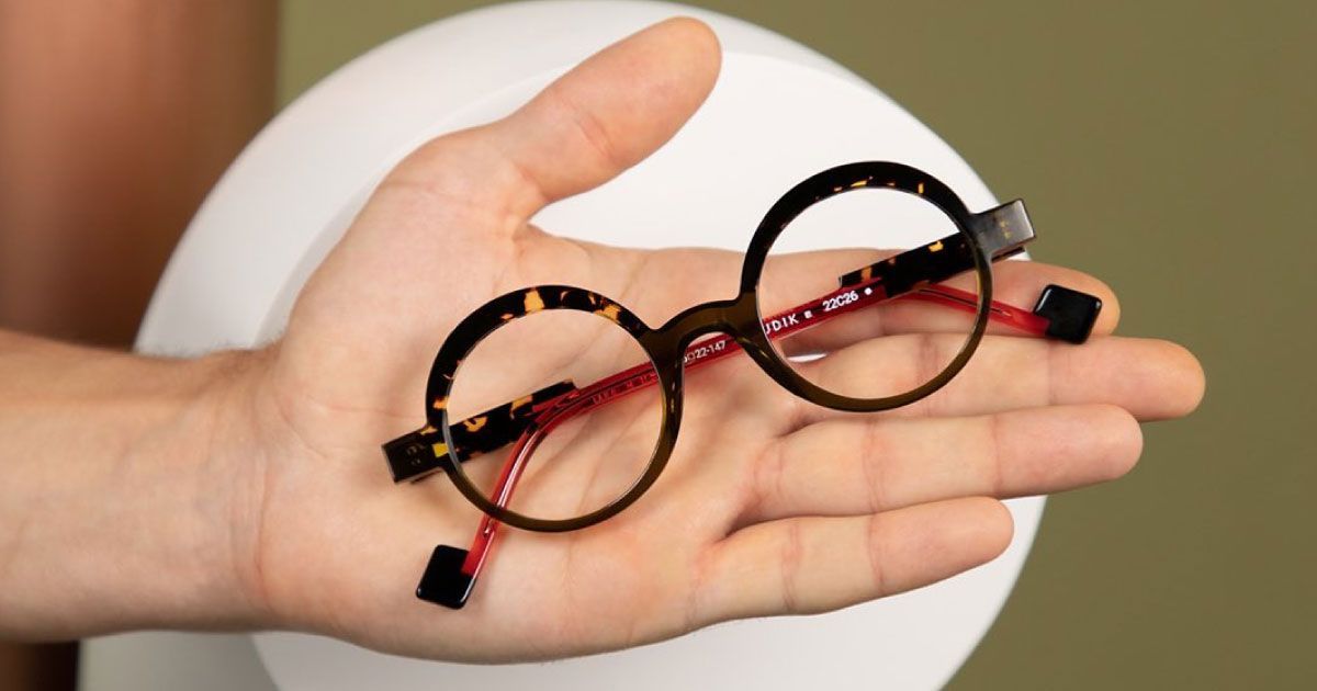 A person is holding a pair of round-shaped glasses in their hand.