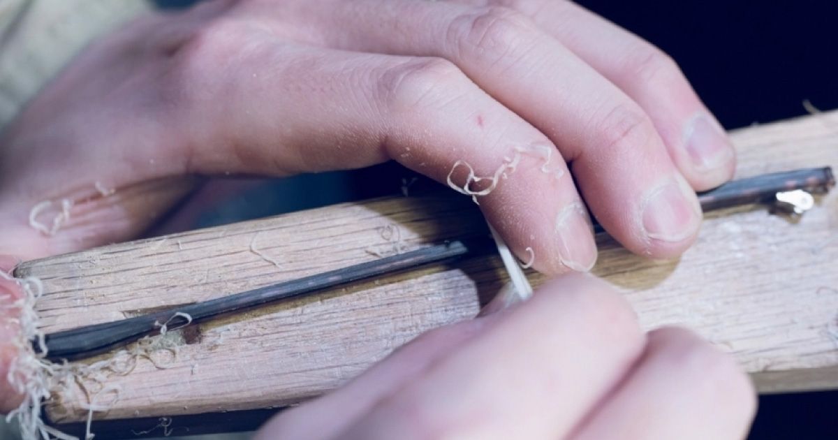 Closeup of hands working on an eyewear temple with a tool creating white acetate shavings.