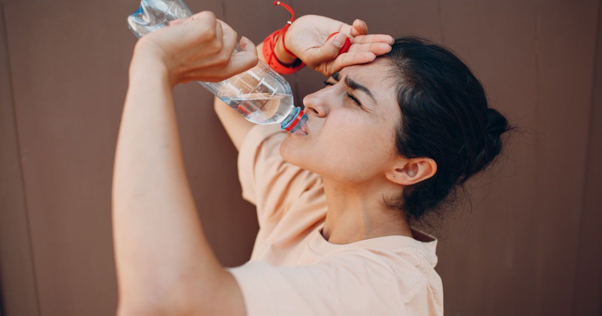 A woman is drinking water from a plastic bottle.