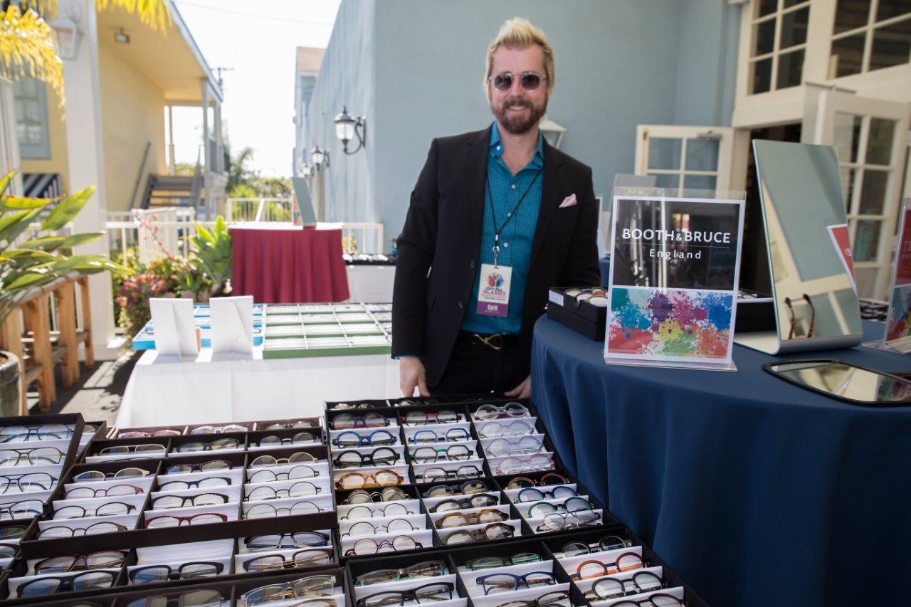 Vendor wearing sunglass frames at outdoor table at Raise Your Glasses 2018 Event