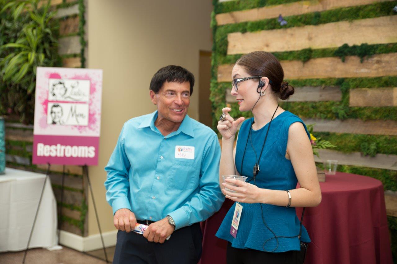 2 people standing indoors and talking at Raise Your Glasses 2018 Event