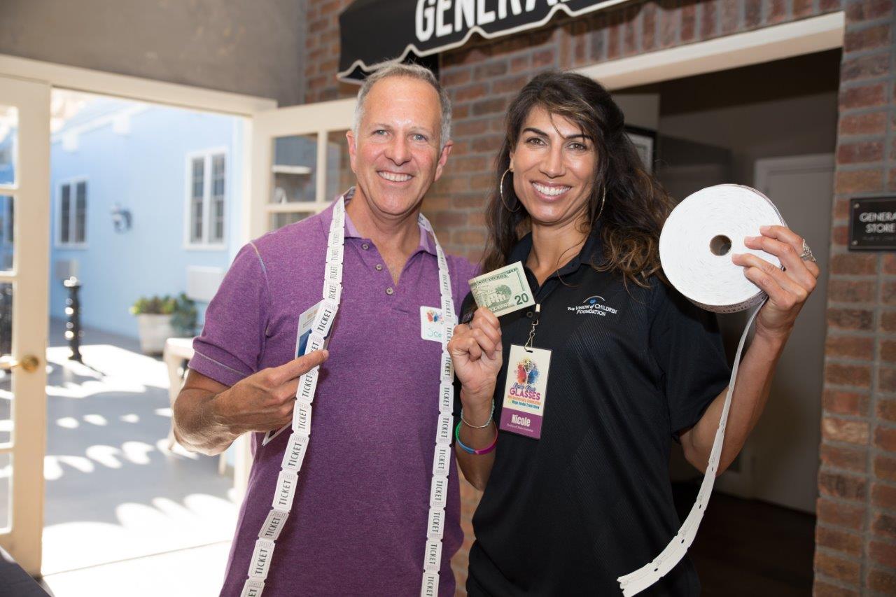 Two people holding long strands of drawing tickets and smiling during Raise Your Glasses 2018 Event