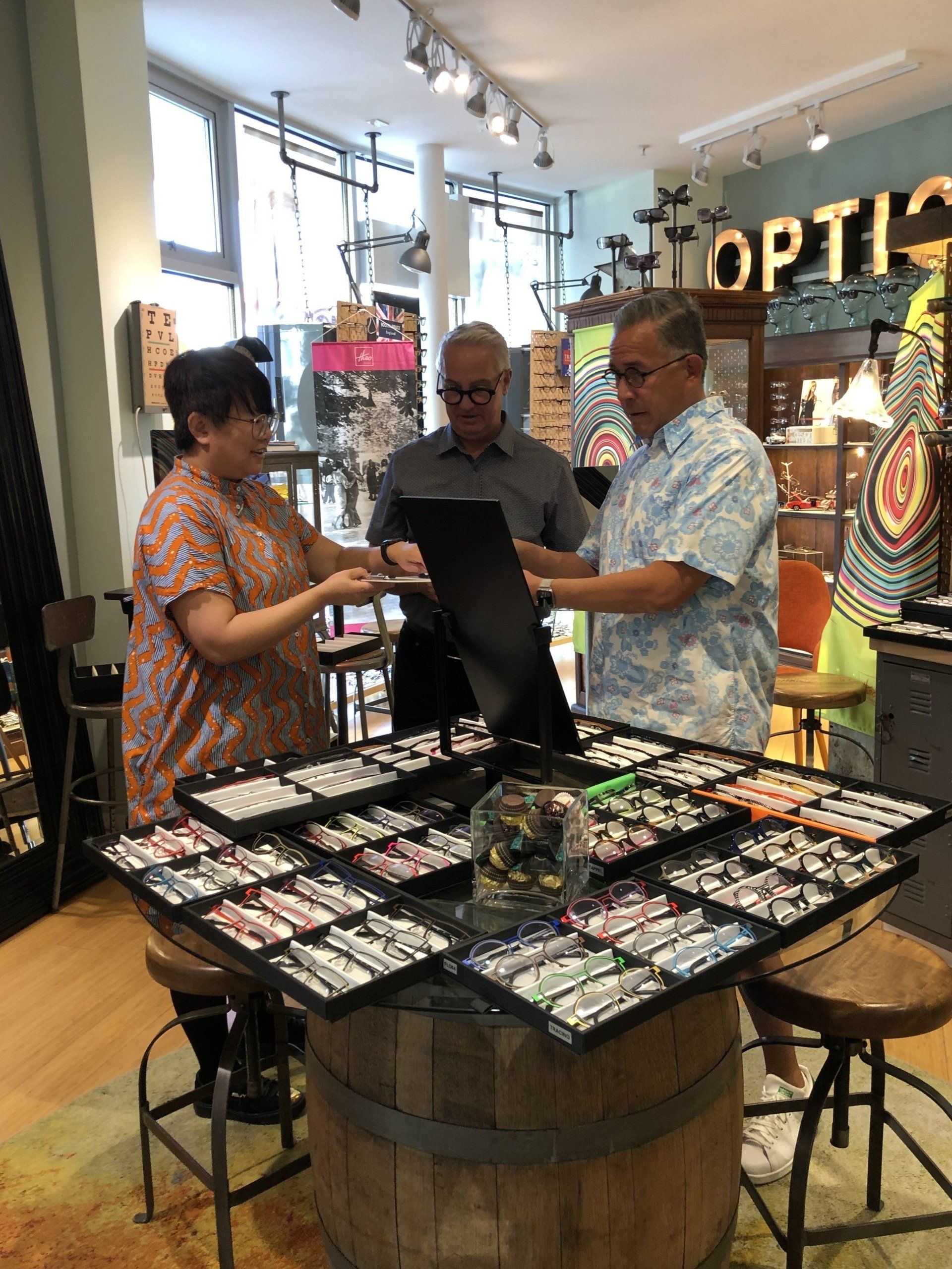 Three people standing inside looking at frames at Theo Trunk Show Event