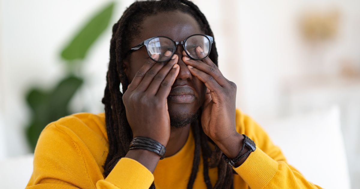 A man wearing glasses is rubbing his eyes with his hands.