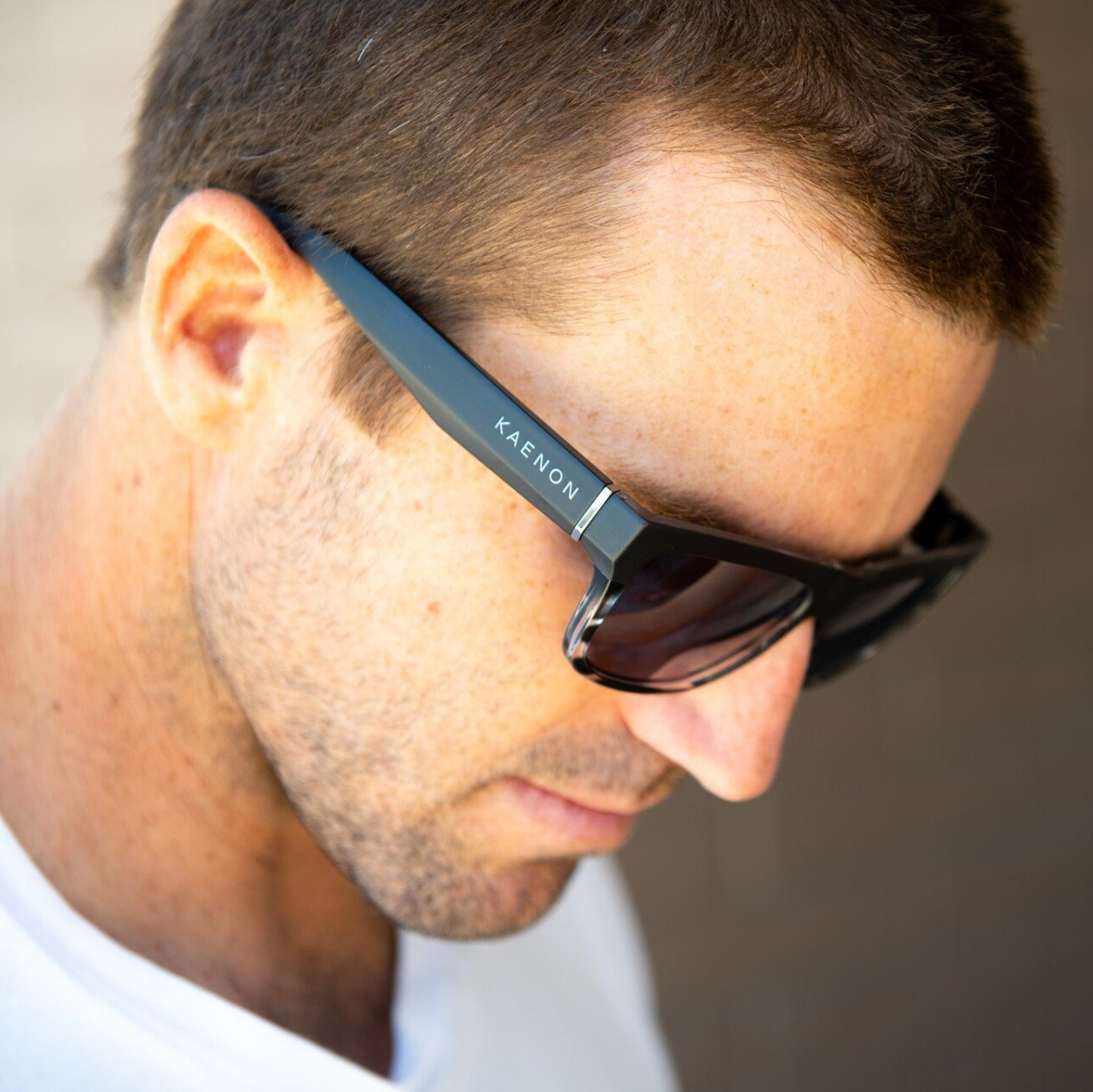 Man looking down wearing a black pair of Kaenon sunglasses
