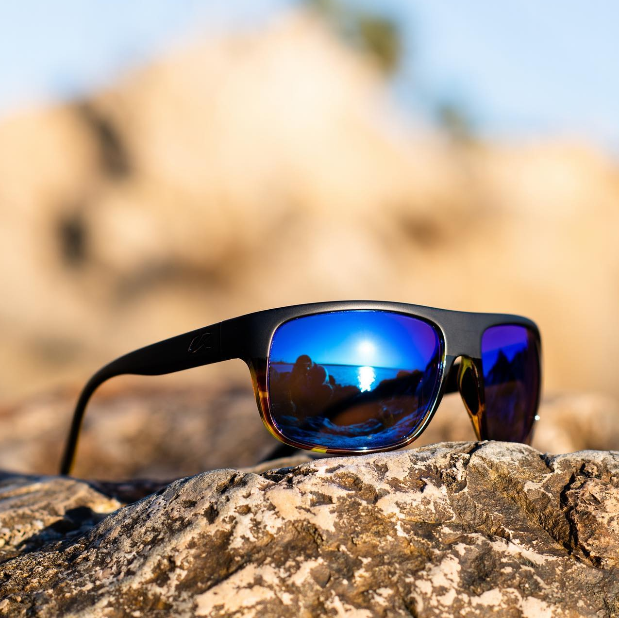 Pair of Kaenon wraparound sunglasses in tortoise with blue mirror glasses sitting on a rock