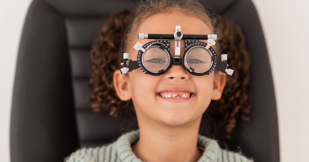 A young girl is sitting in a chair wearing trial glasses during an eye exam.