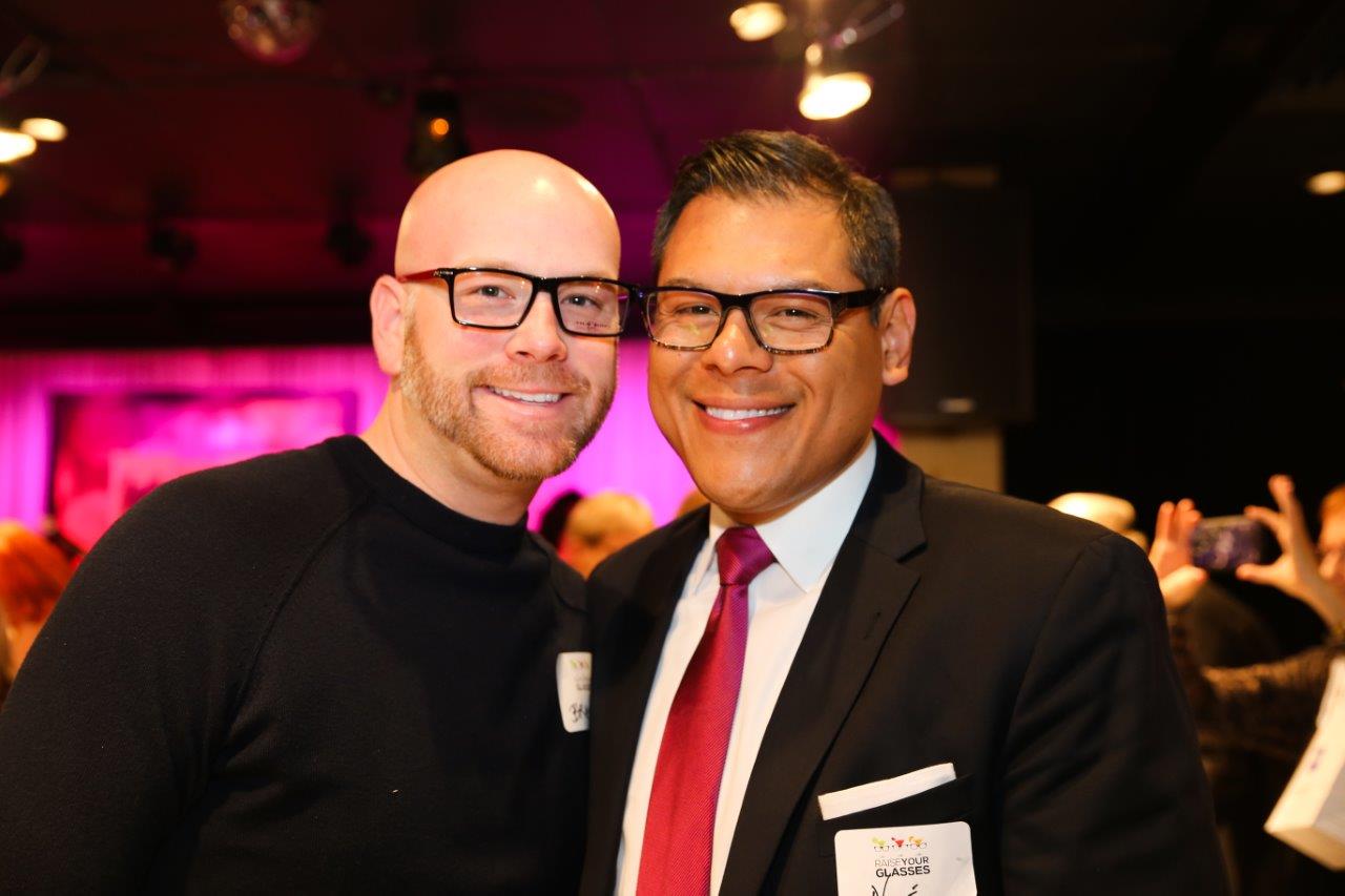 Two guests standing inside and smiling at Raise Your Glasses event