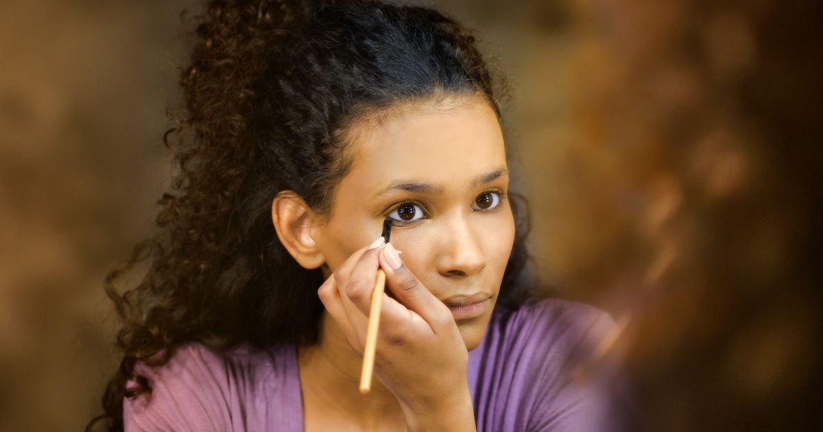 A woman is applying eye shadow in front of a mirror.