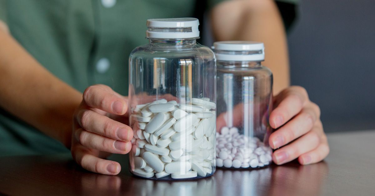 Person holding two glass pill bottles filled with white pills.