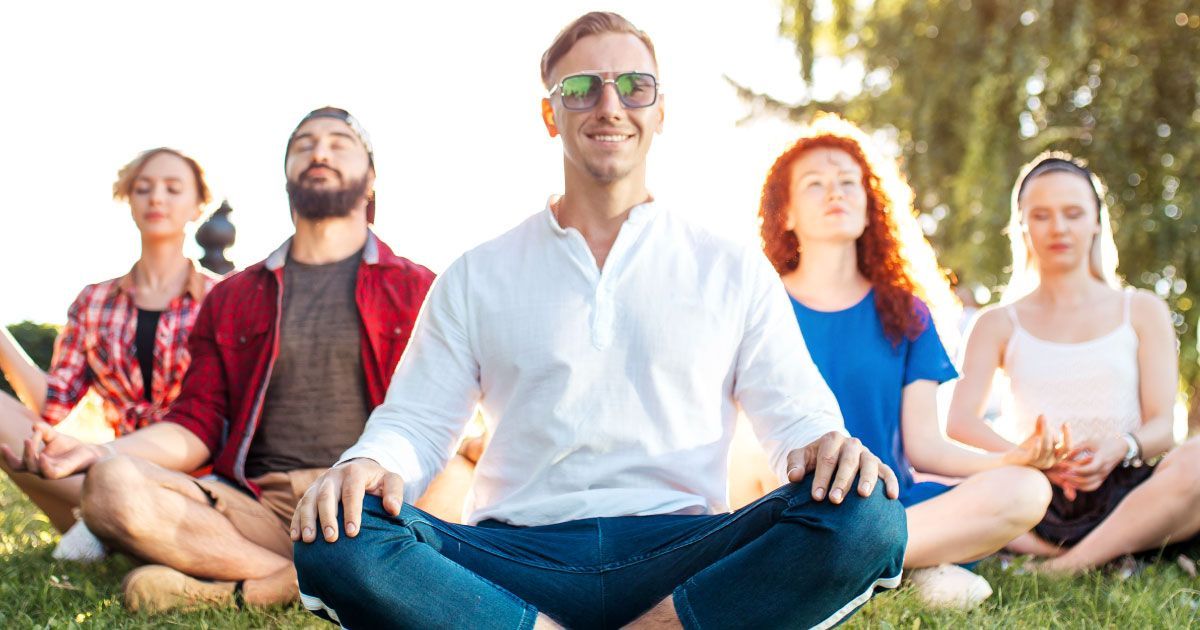 A group of 5 people are meditating on the grass in a park.