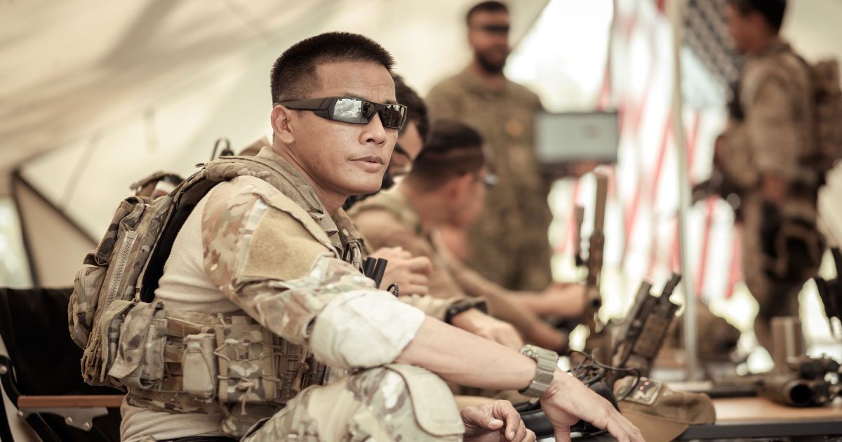 A soldier wearing sunglasses is sitting in a tent with other soldiers.