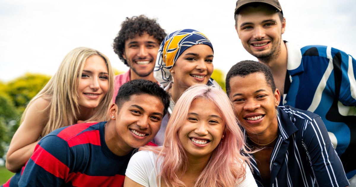 A group of multicultural young people posing for a picture together in a park.