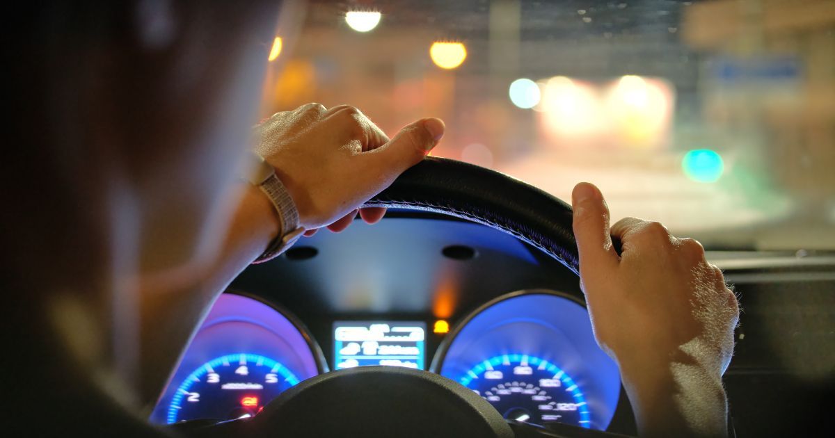 A person is driving a car at night with their hands on the steering wheel .