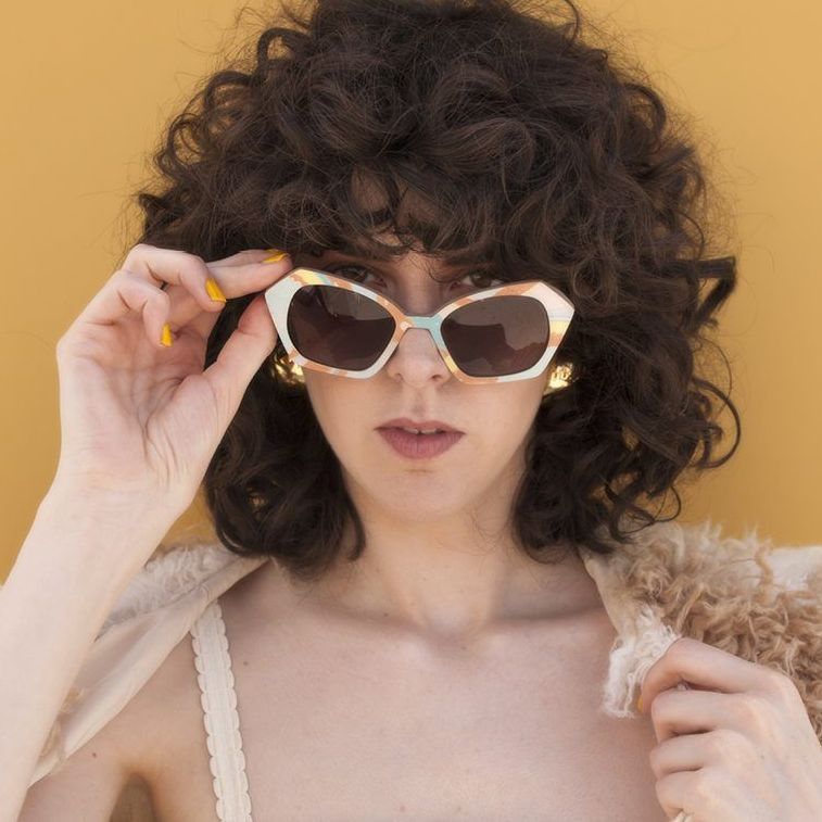 A woman with curly hair wearing nina mur sunglasses and earrings
