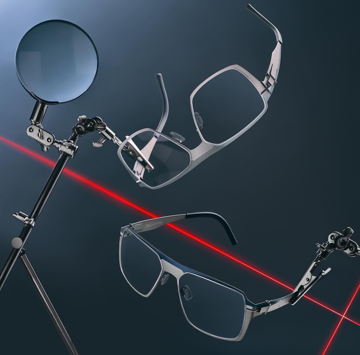 Two pairs of silver glasses clipped onto a stand with a magnifying glass